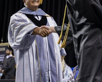 Regent Gallegos shakes the hand of a UCCS graduate